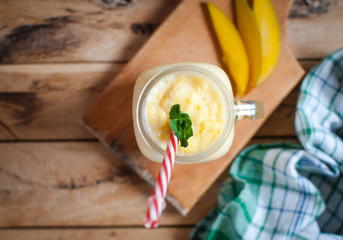 Mango smoothie in a jar on wooden table, top view