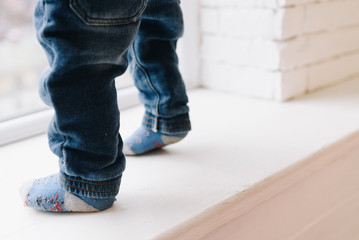 Danger of falling out and child safety issue as baby is standing on a windowsill. Dangerous, unsafe, caution.