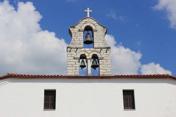 Orthodox bell tower with three bells and large white cross at Greek church blue sky with clouds at the background