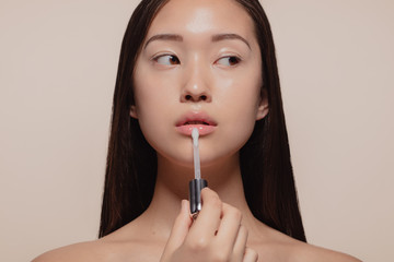 Woman applying transparent lip gloss - obrazy, fototapety, plakaty