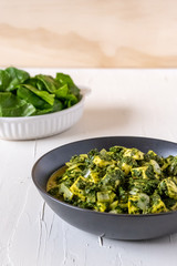 Bowl of spinach paneer on a white table with fresh spinach in the background 