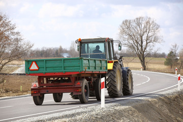 A tractor with a trailer rides on an asphalt road. Rear view of agricultural transport....