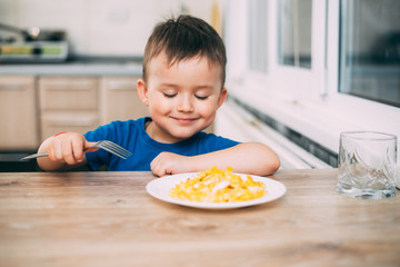 a child in a t-shirt in the kitchen eating an omelet, a fork