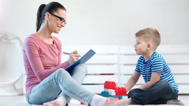 Smiling female kid psychologist watching and taking notes during psychology testing