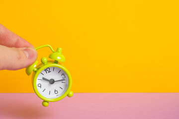 Fingers hold a vintage green clock on a yellow background.