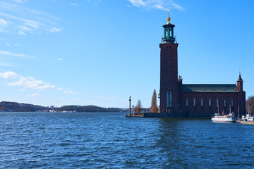 Stockholm city hall in daylight against a blue sky with waves on water.