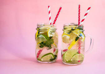 Two jars of tasty cold lemonade on a pink background