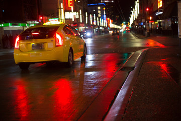Yellow taxi car driving  rain night city wet asphalt red reflections copy space