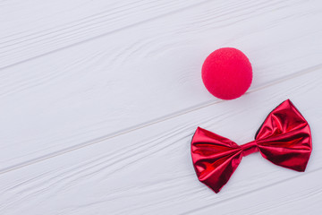 Birthday accessories on white wooden background. Red clown nose sponge and bow-tie and on white...