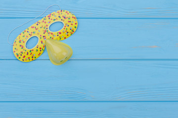 Funny masquerade mask for kids. Yellow clown face mask on blue wood with text space. Kids party...