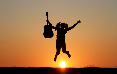Obraz na płótnie Canvas Silhouette of a guitar player at sunset, girl guitarist, silhouette of a guitar, music, girl jumping with a guitar
