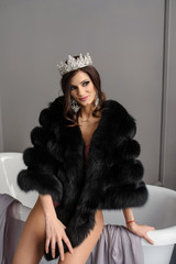 close up photo of a sexy fashion woman in black fur coat and pink underwear with a crown on her...