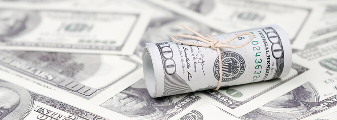US dollars rolled up and tightened with band lies on a lot of american banknotes with blurred...