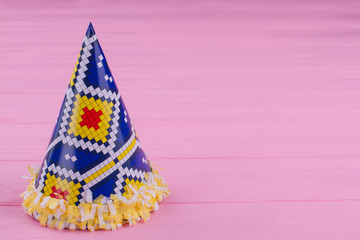 Blue party hat on pink wooden background. Paper cone hat for Birthday celebartion. Color wooden background with copy space.