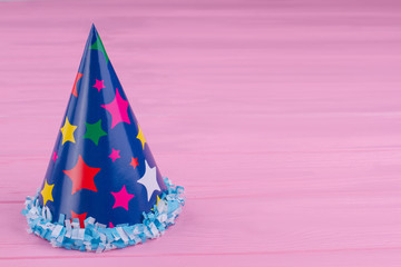 Blue party hat with stars pattern. Cardboard party cap on pink wooden background with copy space.