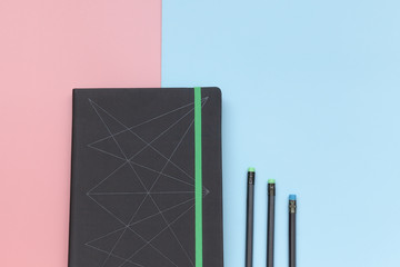 Top view, notebook and pencils on pink and blue background. Close-up