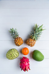 Exotic fresh summer fruits on white background. Dragon fruit, pineapple, persimmon, mango, annona cherimola flat lay with free copy space.