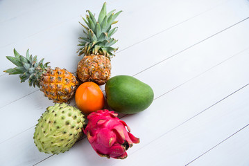Exotic fresh summer fruits on white background. Dragon fruit, pineapple, persimmon, mango, annona cherimola flat lay with free copy space.