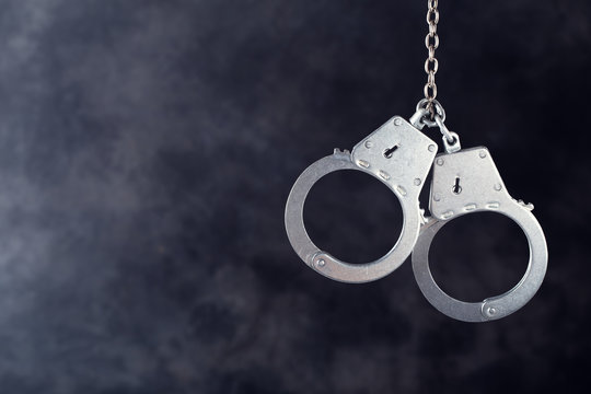 Handcuffs hanging against a dark background with copy space