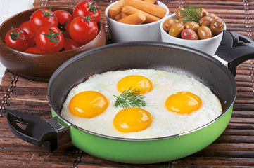 Pan of fried eggs, with cherry-tomatoes and parsley on a wooden table surface.