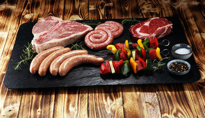Assorted delicious raw meat with vegetable on a barbecue with t-bone steak, sausages and meat...