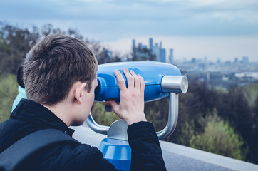 Fototapeta na wymiar The guy is looking through binoculars through the urban landscape on the observation deck.
