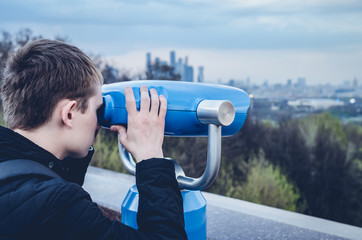 The guy is looking through binoculars through the urban landscape on the observation deck.