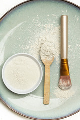 Top view of cosmetic clay powder in a bowl with a spoon and cosmetic brush