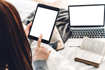Naklejka premium Woman relaxing and using digital tablet computer with white mockup blank screens on the bed at home.woman checking social apps and working..Communication and technology concept