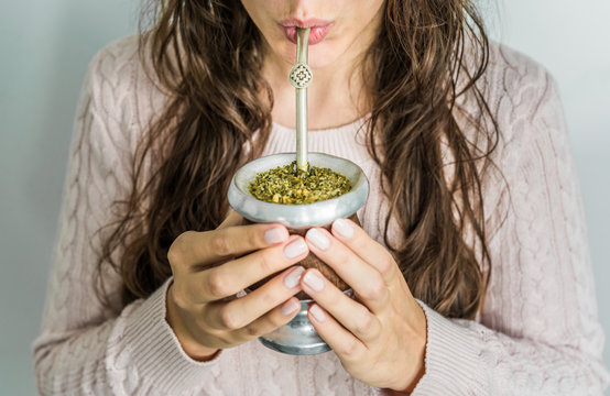 Young woman drinking traditional Argentinian yerba mate tea from a calabash gourd with bombilla stick 