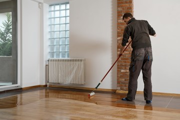 Lacquering wood floors. Worker uses a roller to coating floors.