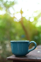 green mug of hot drink put on wooden table in nature of morning day