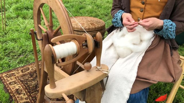 4K HD video close up on spinning wheel with woman in old colonial dress creating thread from wool. The treadle wheel is powered by the spinner's foot rather than their hand or a motor.