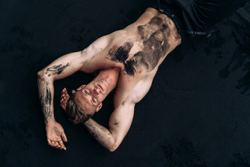 Obraz na płótnie Canvas Top view portrait of muscular sexy guy shirtless lying on black sand beach