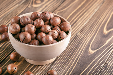 Macadamia nuts in a wooden bowl on a wooden background with copy space.