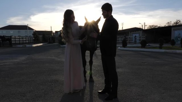 tremendous girl silhouette in long dress and man in black suit pet horse against bright sunset slow motion