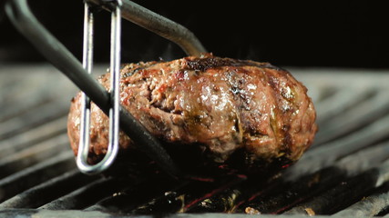 A big juicy burger cutlet is turned over with grinder tongs