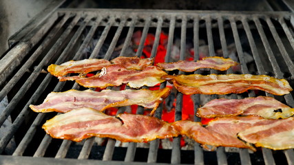 Eight slices of bacon lie on the roasted grill reach their readiness, braised coals and light smoke