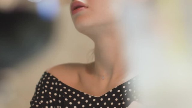 young woman in an evening dress in a cafe through glasses she touches her hands on her shoulders and collarbone