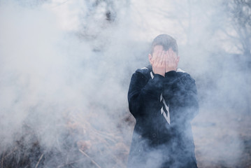 Boy covered his face with a hands in thick smoke. Child safety concept