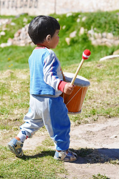 Little latin boy playing drum outside.
