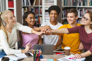 Group of students putting their hands up together in library