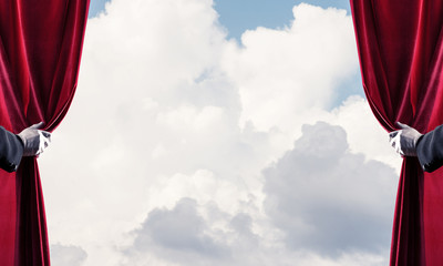 Cloudy landscape behind red curtain and hand holding it