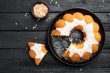 Homemade bundt cake with icing and decorations on black wooden background.