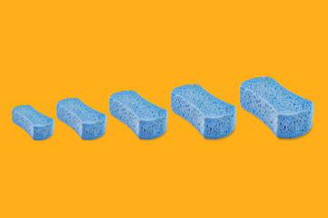 Row of porous blue sponges from small to large on yellow background
