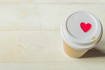 disposable craft paper coffee cup and red wooden heart on a cap. Coff to go on wooden table