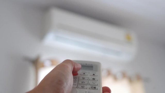 Hand using remote control closing air conditioner in bedroom in the morning. Saving energy