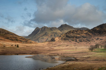 Beautiful vibrant sunrise landscape image of Blea Tarn in UK Lake District with Langdales Range in background