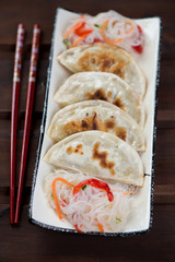 Plate with fried korean potstickers over dark brown wooden background, vertical shot