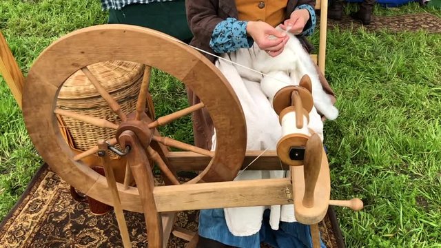 HD video close up on spinning wheel with woman in old colonial dress creating thread from wool. Normal speed slowing to slow motion to show detail of motion. Dramatic transition.